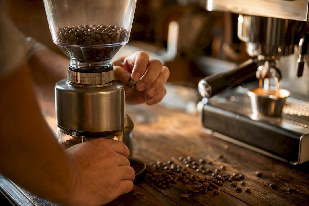 Manos ajustando el molinillo de café para calibrar el espresso