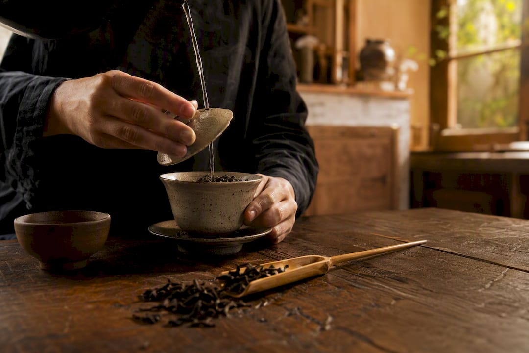 Manos vertiendo agua caliente en un gaiwan de Pu-Erh