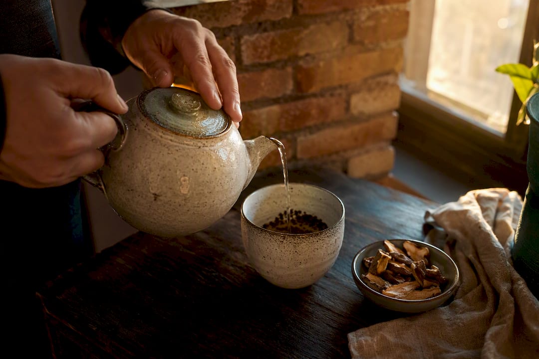 Manos sirviendo café con hongos en una taza de vidrio