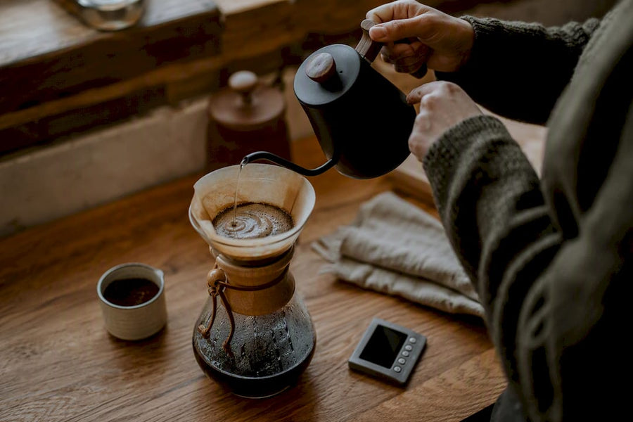 Mains versant de l'eau sur du café moulu dans une Chemex